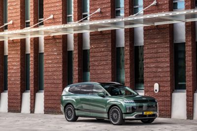 Hyundai IONIQ 9 geparkeerd voor een gebouw en aangesloten op een laadpunt.