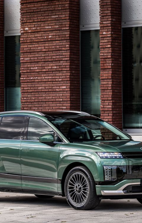Hyundai IONIQ 9 geparkeerd voor een gebouw en aangesloten op een laadpunt.