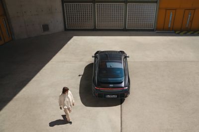 En mann går forbi en parkert Hyundai IONIQ 6 i sort sett ovenfra. Foto.