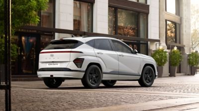 Hyundai KONA Electric Pure Edition driekwart van achteren in straat met gebouw op achtergrond.