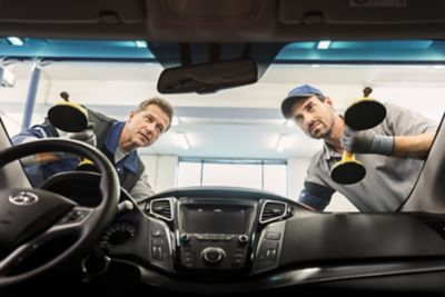 Dwóch ekspertów serwisowych ASO Hyundai wymienia szybę w samochodzie