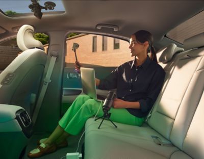 Woman with green trouser smiles into her phone while in charging her laptop on the Hyundai IONIQ 6