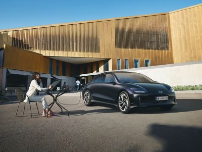 The Hyundai IONIQ 6 all-electric sedan parked in front of building with woman sitting next to it.