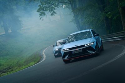 Two Hyundai IONIQ 5 N high-perfomance EV driving on a curvy racetrack with trees. 