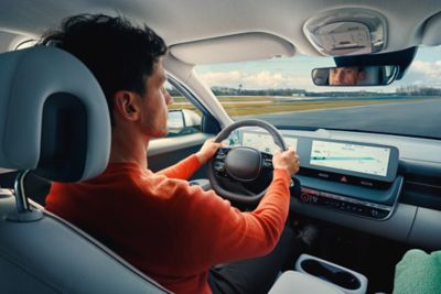 A woman sitting behind the wheel of her Hyundai KONA, looking very relaxed.	