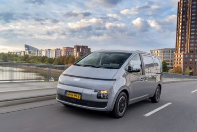 Driekwart vooraanzicht Hyundai STARIA Cargo rijdend over een brug in de stad.