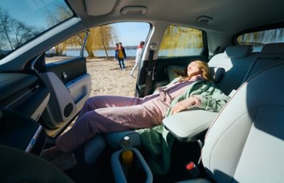 Eine Frau liegt entspannt auf dem zurückgeklappten Beifahrersitz des IONIQ 5. Die Sonne fällt durch die offene Tür herein.