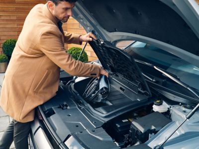 The driver of a Hyundai IONIQ 5 storing the charging cable in the front of the car.