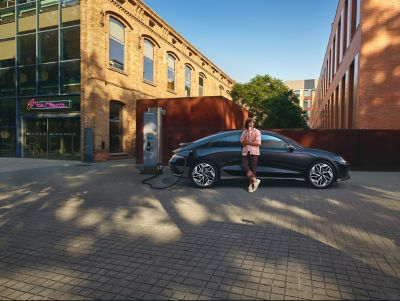 Rueda lateral del Hyundai IONIQ 6 y una mujer con falda verde caminando junto a él.