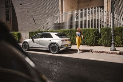 The Hyundai IONIQ 5 EV parked on a city street with a woman walking away from it.