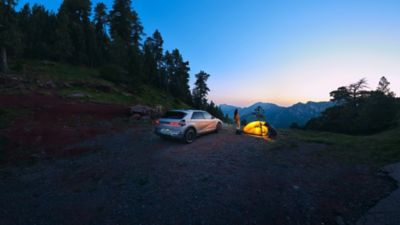 Eine Familie campt mit ihrem vollelektrischen Hyundai IONIQ 5 und einem aufgeschlagenem Zelt in den Bergen.