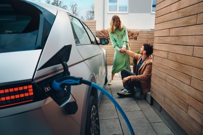 The Hyundai IONIQ 5 electric midsize CUV charging at home, a young couple sitting next to it.