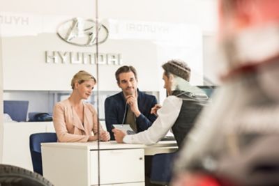 Ein Mitarbeiter eines Hyundai Autohauses berät eine Frau und einen Mann an seinem Schreibtisch.  