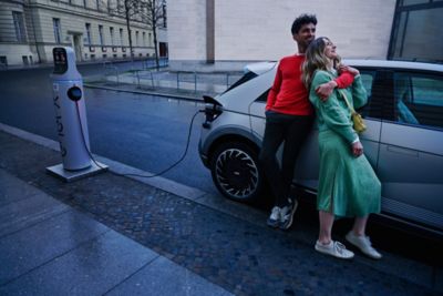 A young couple standing next to their Hyundai IONIQ 5 as it is charging in a residential city street.