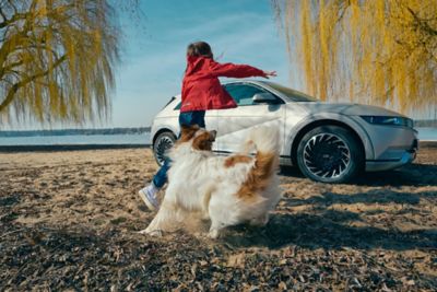 Hyundai IONIQ 5 electric vehicle parked at a lake with a girl playing fetch with a dog.