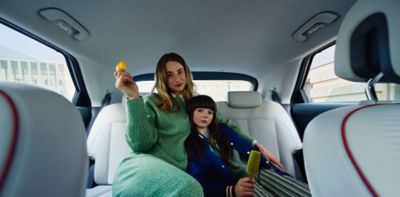 Eine Frau sitzt lächelnd auf der Rückbank eines Autos neben einem kleinen Mädchen. Beide halten ein Eis in ihrer Hand.
