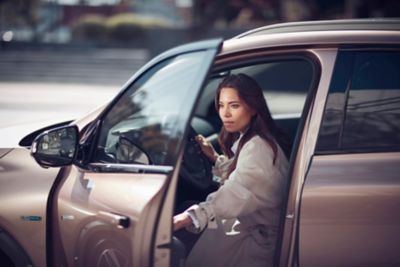 A woman getting into the driver's seat of a Hyundai NEXO hydrogen fuel cell vehicle.