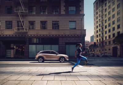 A woman with a prosthetic lower right leg running past a Hyundai Nexo hydrogen fuel cell SUV.