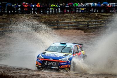 Hyundai Motorsport rally car i20 R5 driving through big puddle spraying water out 4 metres.