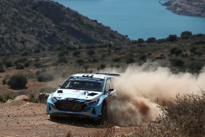 Samochód rajdowy Hyundai Motorsport i20 R5 w akcji na szutrowej drodze.
