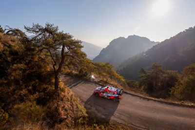 Hyundai i20 N WRC rajdowy samochód wyścigowy jadący pod górę po krętej drodze w górach..