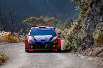 Hyundai i20 N WRC rajdowy samochód wyścigowy jadący szybko po panoramicznej trasie.