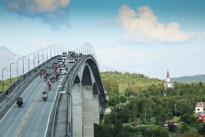 En lang rekke syklister syklende over en bru i Arctic Race of Norway 2024. Foto.