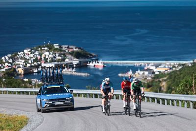 Arctic Race of Norway 2025 – En lang Følgebil og tre syklister i et fantastisk landskap4. Foto.