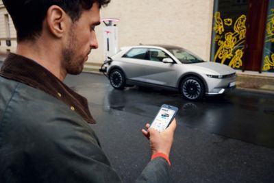 Man walking towards the Hyundai IONIQ 5 electric vehicle using the Bluelink app on his smartphone.