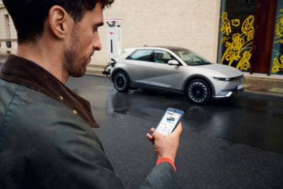 A man, looking at his cell phone while he approaches his Hyundai IONIQ 5 parked in the street.