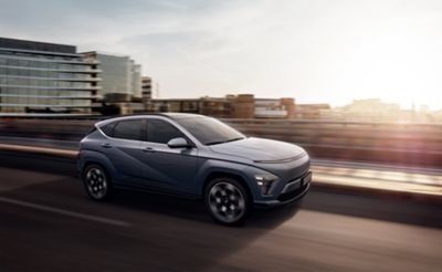 De all new Hyundai KONA is van opzij gefotografeerd terwijl hij door een stadsstraat rijdt. 