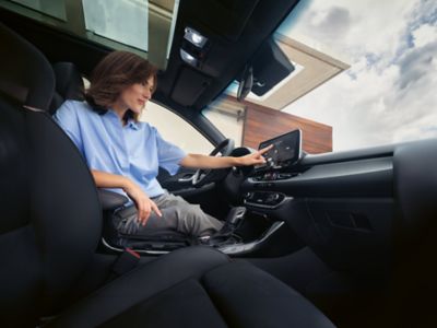 Une femme assise sur le siège du conducteur, utilisant l'écran tactile multimédia sur le tableau de bord.