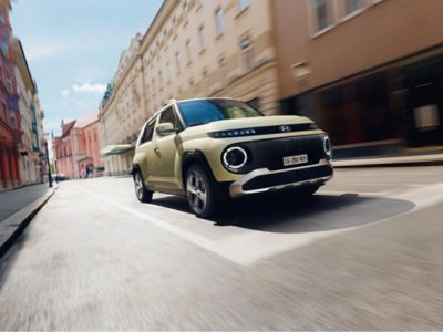 La Hyundai INSTER percorre una strada cittadina interna, fiancheggiata da edifici ravvicinati su entrambi i lati.