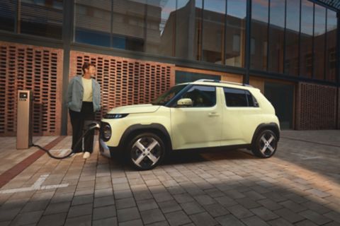 Person stands next to the INSTER while it charges at a public charging station in an urban plaza.