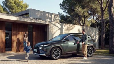 TUCSON Plug-in Hybrid parkerad utanför ett modernt hus, familj i rörelse runt bilen.