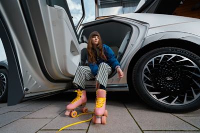 A woman wearing pink rollerskates sitting in the rear door of the Hyundai IONIQ 5 electric midsize CUV.