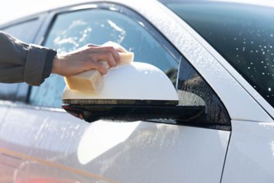 Nærbilde av en som vasker speilet med en svamp. foto.