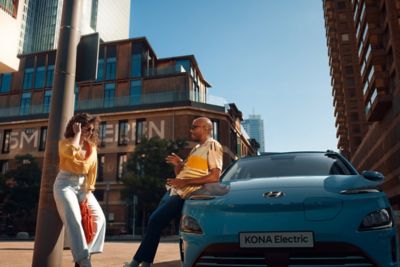 A man leaning against the Hyundai Kona Electric talking to his friend.