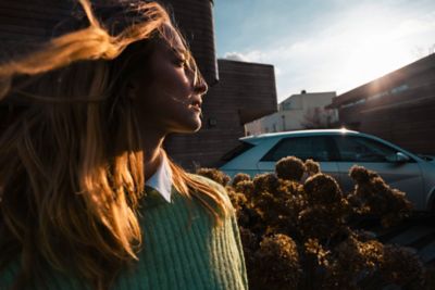 A woman in the sunshine standing next to the Hyundai IONIQ 5 electric CUV.