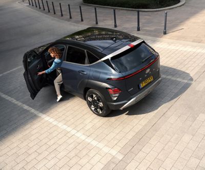 Vrouw opent portier geparkeerde Hyundai KONA Hybrid en stapt uit.