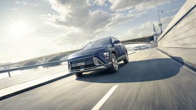 The all-new Hyundai KONA in blue is pictured driving down a city.