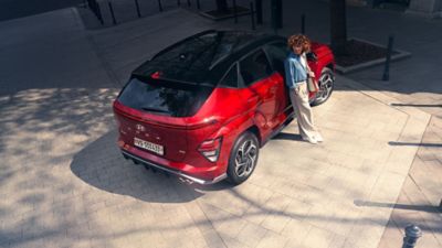 The all-new KONA N Line in red is parked next to a modern building.