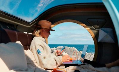 Person i bil sitter vid havet och arbetar vid en dator.
