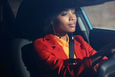 A woman sitting behind the wheel of her Hyundai KONA, looking very relaxed.	