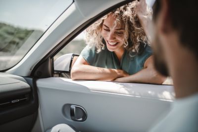 A woman leaning on the passenger's door, talking to the passenger of the Hyundai IONIQ 5 EV.