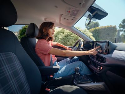 Une femme utilisant l'écran tactile central au volant de la Hyundai i10 arrêté. 