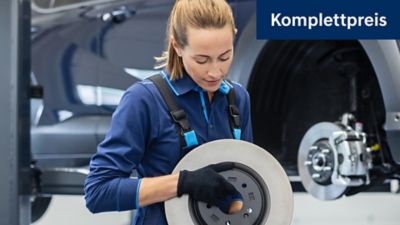 eine Mechanikerin, die eine Bremsscheibe in der Hand hält