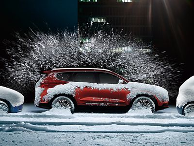 Ein am Straßenrand vor einem Strauch geparkter, teilweise schneebedeckter roter Hyundai.