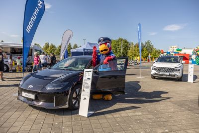 Das Hyundai Verkehrs-Maskottchen, der Papagei Fredi, lehnt an der geöffneten Fahrertür des Hyundai IONIQ 6.