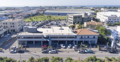 Vista da sopra dell'edificio di concessionaria ed officina con davanti una strada e dietro parcheggio auto